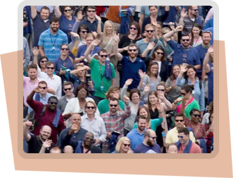 A photo of the Benefitfocus company at a team outing. All pictured are smiling and waving at the camera. They appear to be at an outdoor sporting event. 